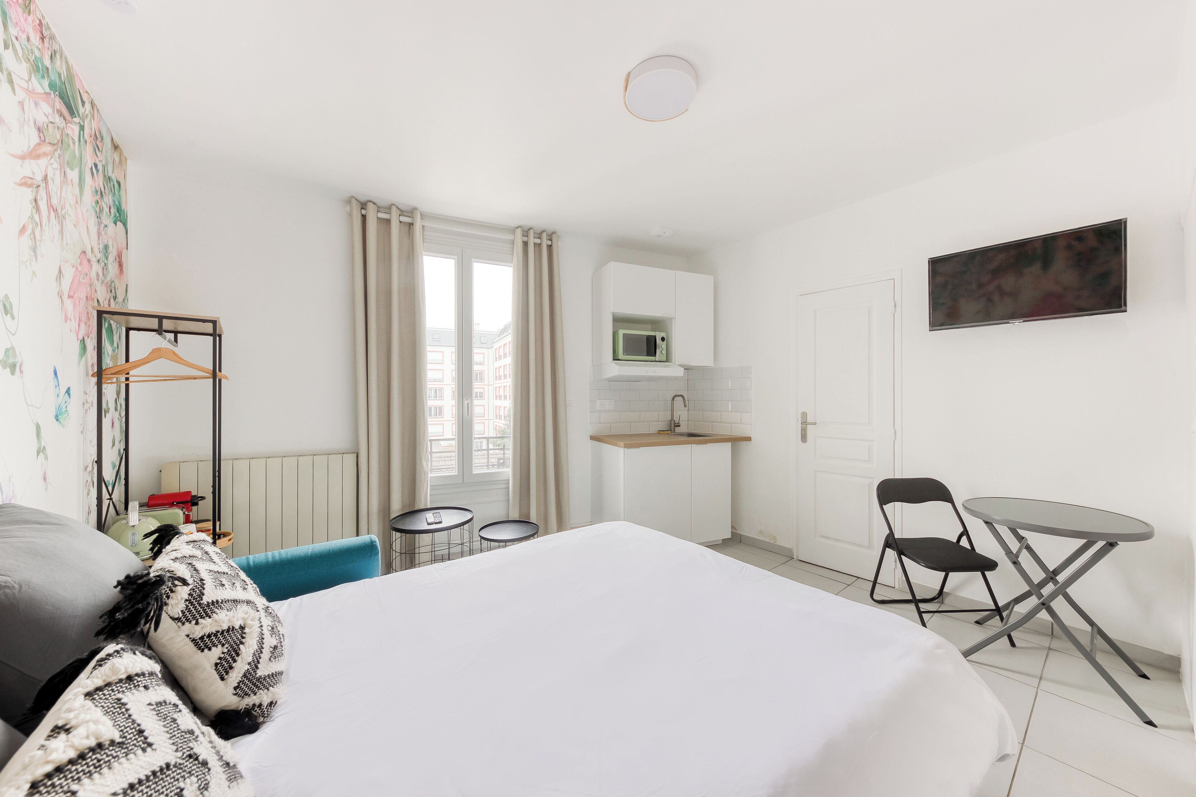 Una habitación de hotel con cama, escritorio con silla, mesita, microondas y ventana con cortinas.