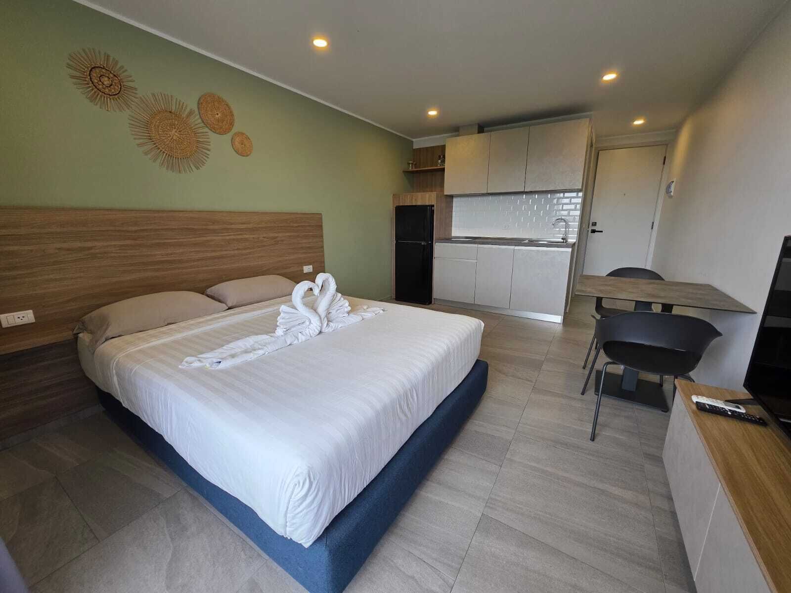 A hotel room with a bed, a desk, a chair, a TV, and a kitchenette.