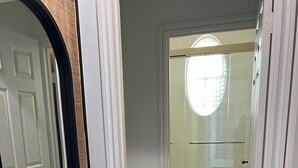 Une salle de bain avec une porte blanche, un miroir avec un cadre en bois, une douche avec une porte en verre et un sol carrelé.