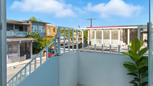 A balcony with a white railing overlooking a street with buildings and a clear sky. - New 3-BR Apartment, A/C, Free Parking, Washer Dryer, Full Kitchen, WiFi (San Juan)