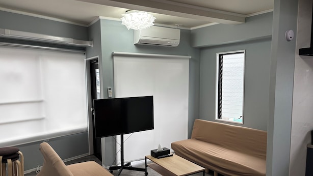 Un salón moderno con un televisor de pantalla plana sobre un mueble bajo, un sofá color beige, una mesa de centro de madera y una ventana con vistas.
