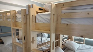 Habitación con literas de madera, ropa de cama blanca y un panel de control en la litera superior.