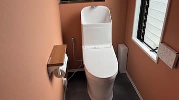 Une salle de bain moderne avec des toilettes blanches, une petite étagère en bois et une fenêtre avec une grille métallique.