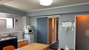 Una habitación de hotel moderna con una mesa de comedor de madera, sillas naranjas, un microondas, un lavabo y un teléfono.