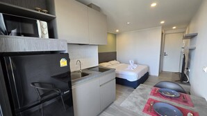 A compact hotel room with a kitchenette, a bed with towels, and a dining area with tableware. - Blue Edge Studio T3-527 (Chalong)