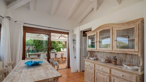 A rustic kitchen with wooden cabinets, a dining table, and a view of the garden through a glass door.