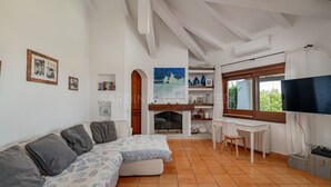 A living room with a sofa, a fireplace, a TV, and a window with a view of greenery.