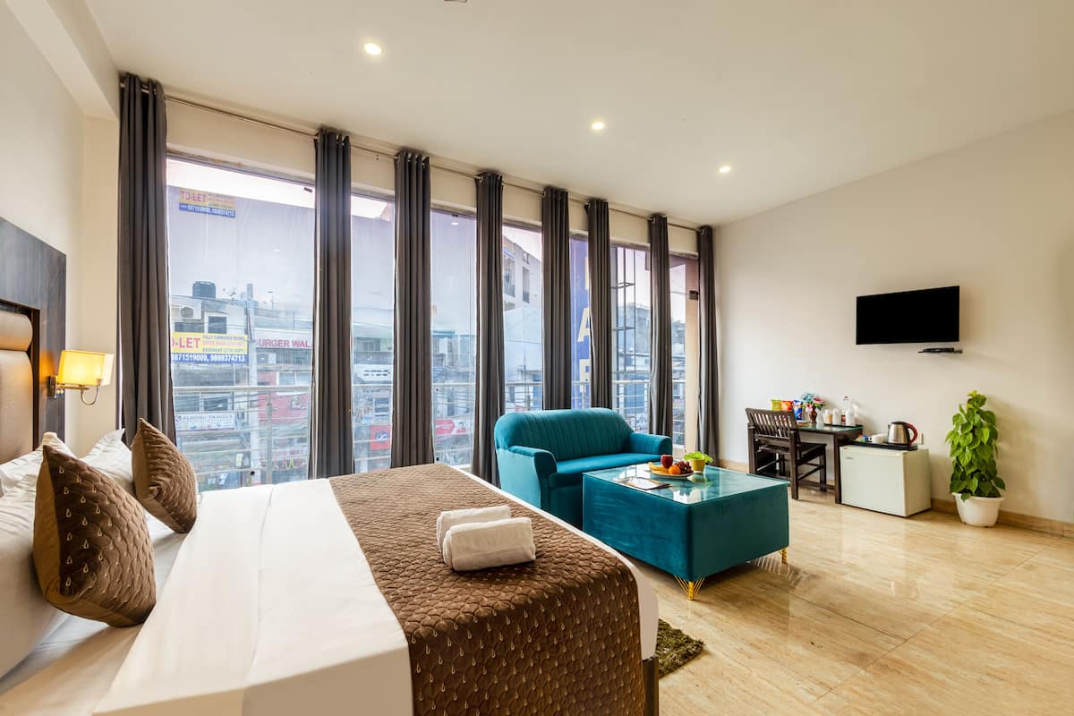 A hotel room with a bed, a sofa, a coffee table, a TV, and a view of the city.