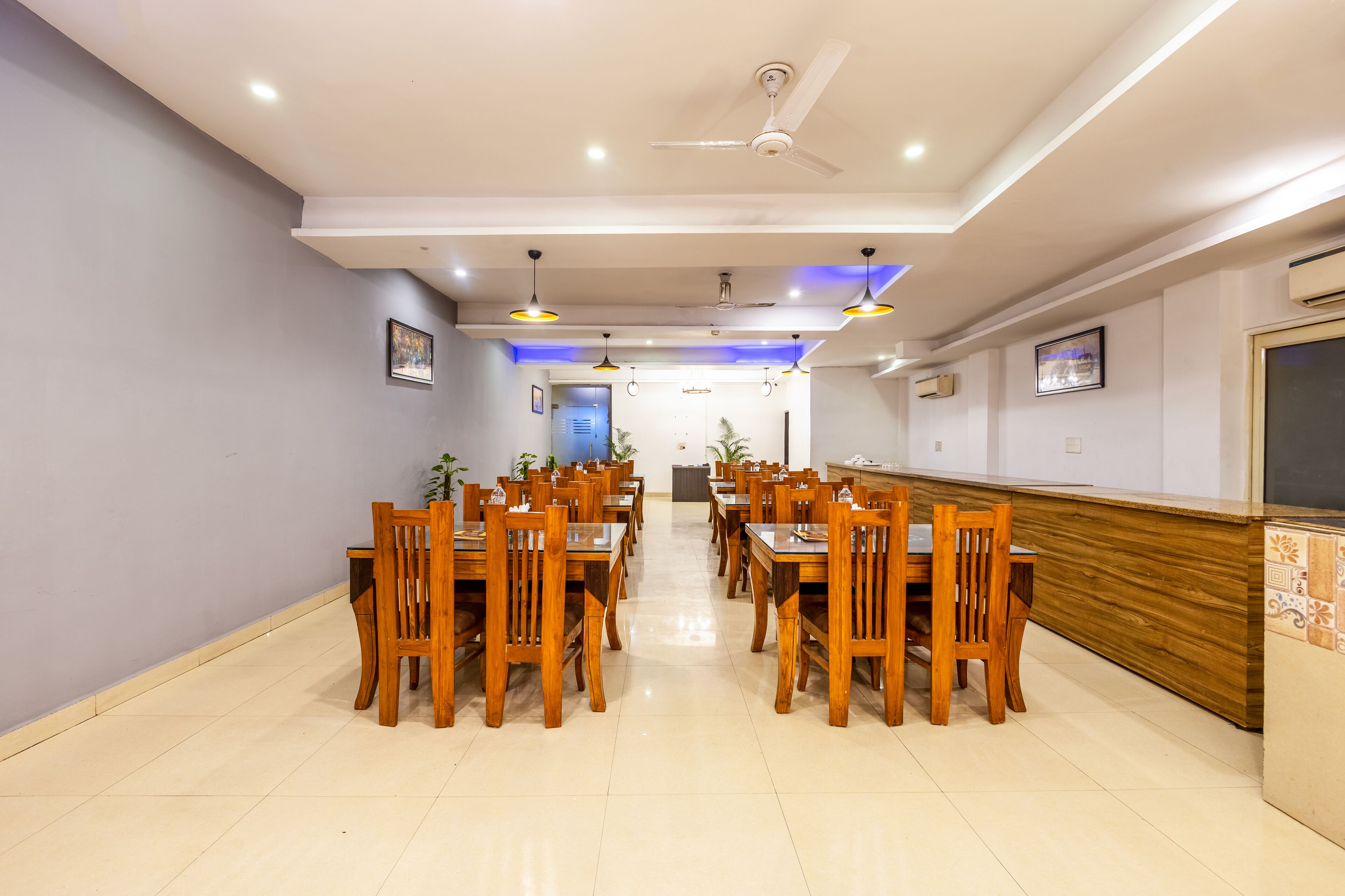 Un comedor amplio con mesas y sillas de madera, iluminación empotrada y ventilador de techo.