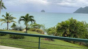 Une vue depuis un balcon donnant sur une plage tropicale, avec des palmiers et une île lointaine.