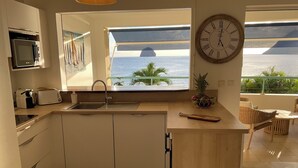Une cuisine avec vue sur l’océan, une horloge et un panier de fruits.
