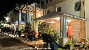 Une rangée de bâtiments d’hôtel avec des patios couverts, des plantes en pot et une allée pavée.