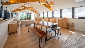 A spacious loft-style room with a wooden dining table, benches, and a sofa. Large windows provide natural light and views of the outdoors. - AR PAVILHON Villa ****, à 50 m de la plage pour un séjour unique à Douarnenez (Douarnenez)