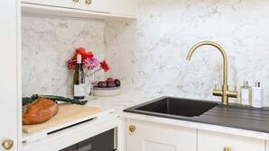 Een keuken met een marmeren spatwand, een zwarte spoelbak met een gouden kraan, en een aanrecht met een mand vol fruit en groenten.