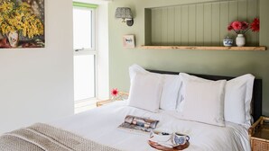 Een opgemaakt bed met witte lakens, een nachtkastje met een lamp en een plank met decoratieve objecten.