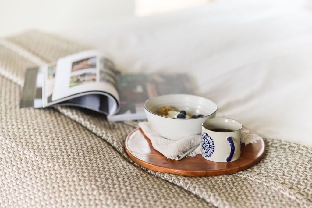 A breakfast setup with a bowl of cereal and a cup of coffee on a wooden tray, placed on a textured fabric surface.