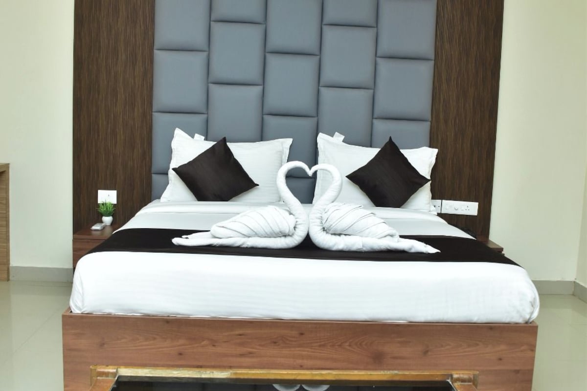 A modern hotel room with a large bed, a wooden headboard, a glass coffee table, and a ceiling fan.