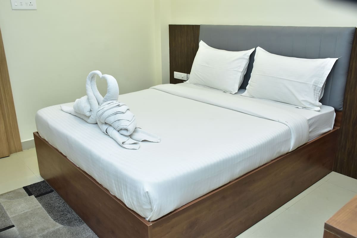 A neatly made bed with white linens and a towel arranged in a heart shape.