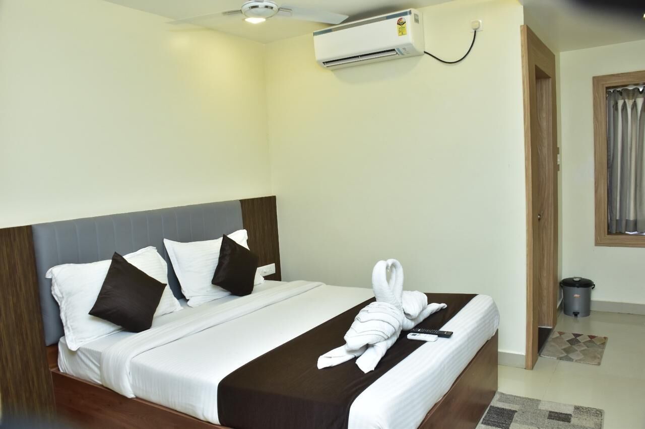Une chambre d’hôtel comprenant un lit, des oreillers, une serviette, une télécommande, un appareil de climatisation, une porte et une poubelle.