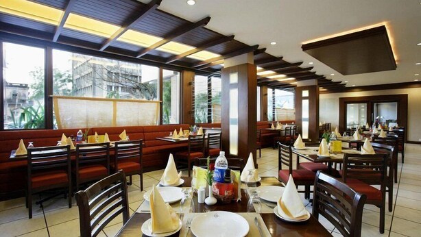 A restaurant with booths and tables, large windows, and a modern ceiling design. -  Safal Exotica Very Close to Sea Beach (Puri)