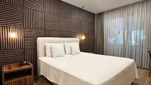 A modern hotel room with a large bed, wooden panel wall, and a nightstand. - Casa Kawa (Arsuz)
