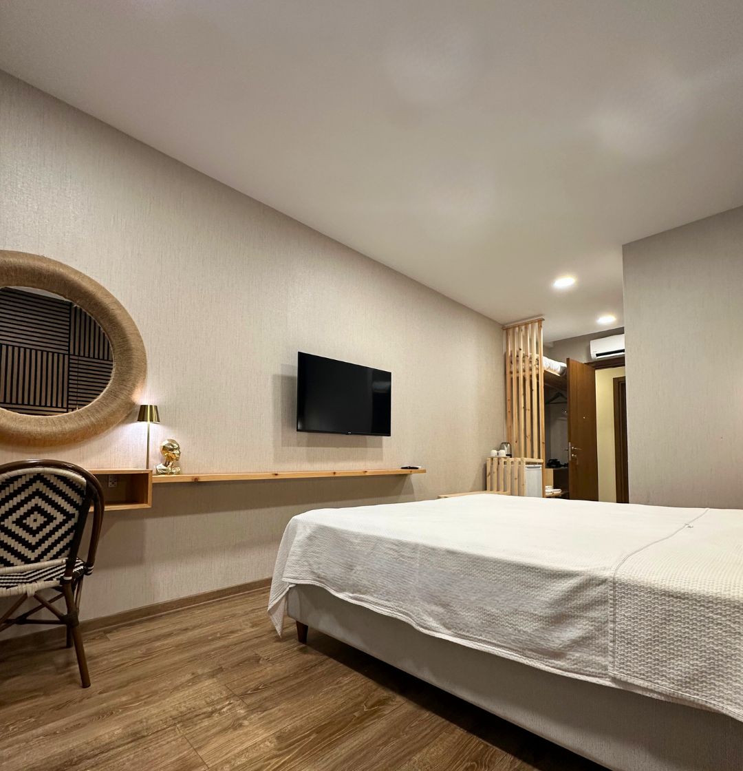 A hotel room with a bed, a desk with a chair, a television, and a circular mirror on the wall.