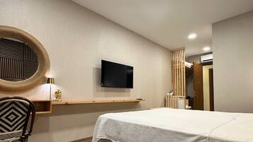 Habitación de hotel con cama, escritorio con silla, televisor y un espejo circular en la pared.