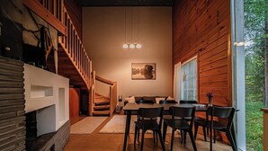 Ein modernes Interieur mit einer Holztreppe, einem Essbereich mit Tisch und Stühlen sowie einem großen Fenster mit Blick ins Grüne.