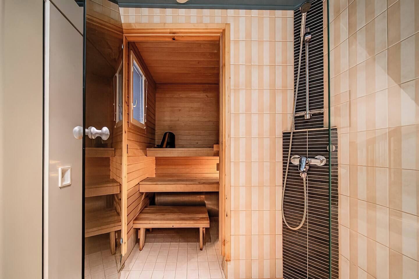 Een sauna met houten banken en een glazen deur, een betegeld douchegedeelte, en een houten deur met een handvat.