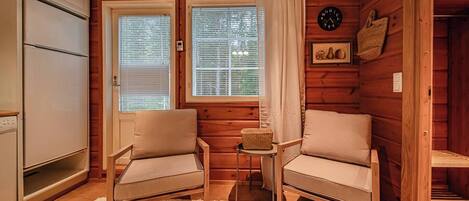 Een gezellig kamer in een chalet met twee stoelen, een kleine tafel, een koelkast en een klok aan de muur.