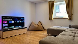 A modern living room with a flat-screen TV, a sofa, a bean bag, and a window with curtains.