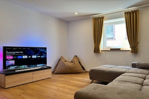 A modern living room with a flat-screen TV, a sofa, a bean bag, and a window with curtains.