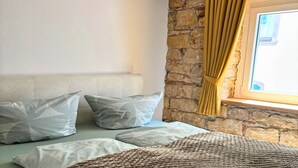 A bed with pillows, a woven blanket, a stone wall, and a window with curtains.