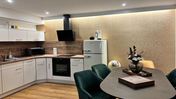 A modern kitchen with white cabinets, a black microwave, a white refrigerator, and a dining area with green upholstered chairs and a table.