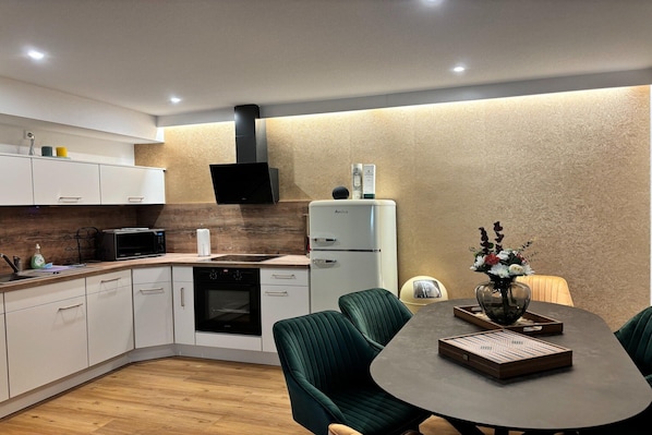 A modern kitchen with white cabinets, a black microwave, a white refrigerator, and a dining area with green upholstered chairs and a table.