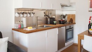 Une cuisine compacte dotée d’un plan de travail en bois, d’appareils électroménagers en acier inoxydable et d’un porte-ustensiles suspendu.