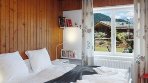 Une chambre à coucher avec un lit, des oreillers, une table de chevet avec des livres, une fenêtre donnant sur une vue de montagne et un radiateur.