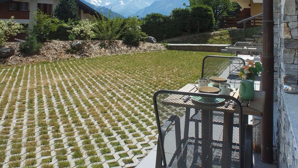 A patio with a view of mountains, a table with chairs, and a stone wall.