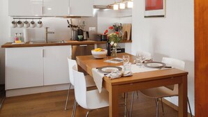 A modern kitchen with white cabinets, a wooden dining table, and a red abstract painting on the wall.
