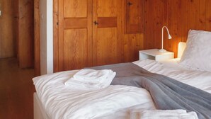 A bedroom with a bed, white linens, a bedside lamp, and wooden paneling.