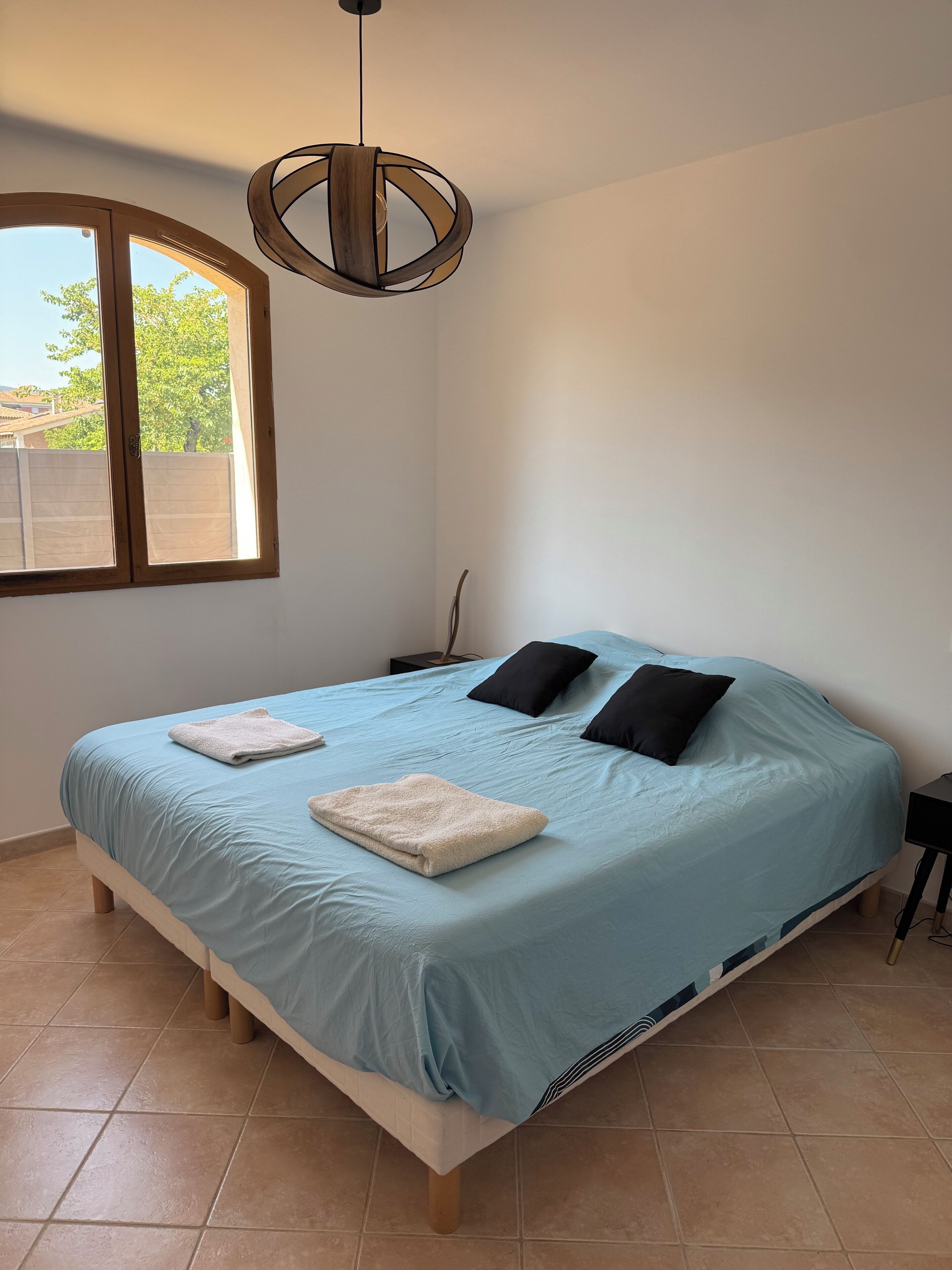 Quarto com cama, duas almofadas, mesa de cabeceira e luminária pendente.