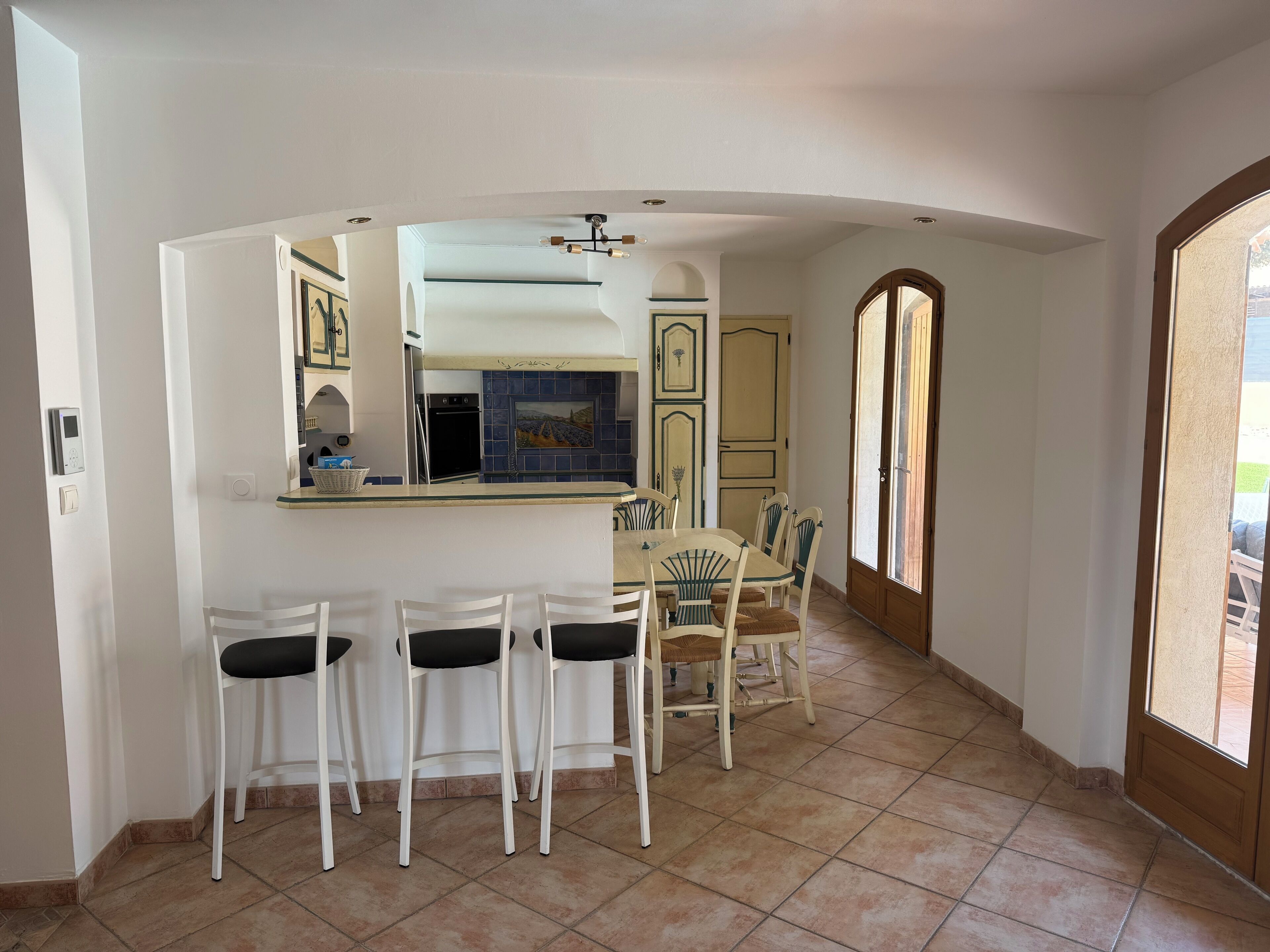 A kitchen with a dining area, featuring a bar counter, chairs, and a tiled floor.