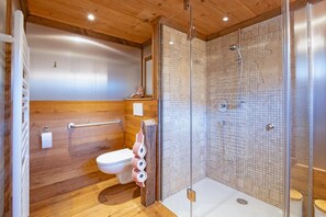 Ein modernes Badezimmer mit Holzboden, einer Glaskabine zur Dusche und einer weißen Toilette.