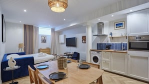 Une chambre d’hôtel moderne équipée d’un lit, d’une table à manger pour deux personnes, d’un coin cuisine et d’un lave-linge.