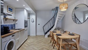 Une cuisine moderne équipée d’un lave-linge intégré, un coin repas avec une table et des chaises en bois, et un escalier en colimaçon.