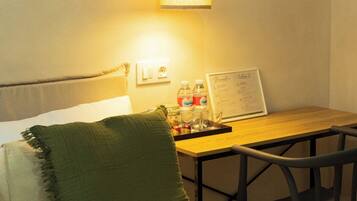 Habitación de hotel con una cama, una mesa de madera con un menú, un cojín verde y una lámpara colgante.