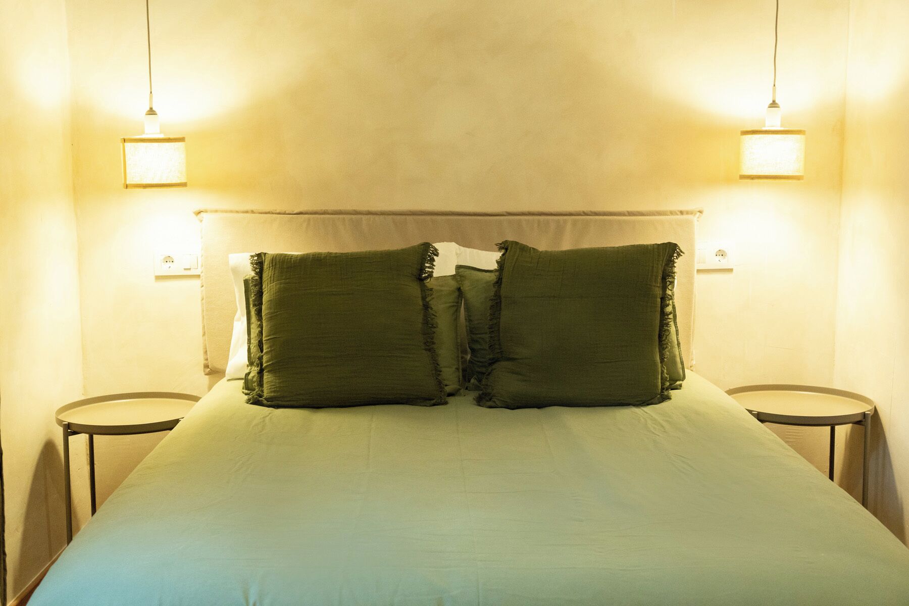 Una cama con dos almohadas, dos mesitas de noche y dos lámparas de pared.