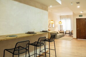 A modern hotel room with a wooden bar area, a sofa, and a dining table with chairs. - Tierra Blanca  (Madrid)