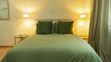 Una cama bien hecha con ropa de cama verde, dos lámparas de noche y una mesita de noche pequeña con un jarrón blanco.