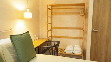 Une chambre d’hôtel avec un lit superposé, un petit bureau avec une chaise, une étagère en bois avec des serviettes et une porte en bois.